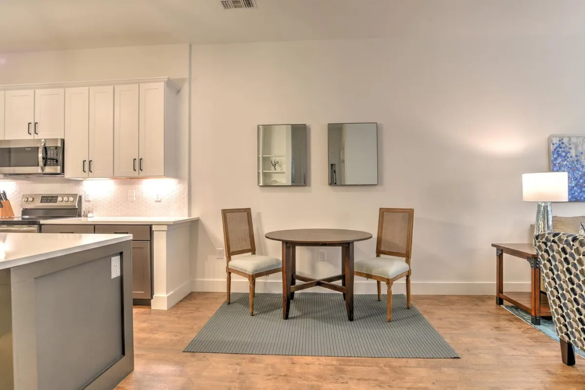 A welcoming dining area with a round table set for two, open to a modern kitchen and accented by mirrors. The scene suggests casual coffee breaks or intimate meals, reflecting the ease and convenience of city living.