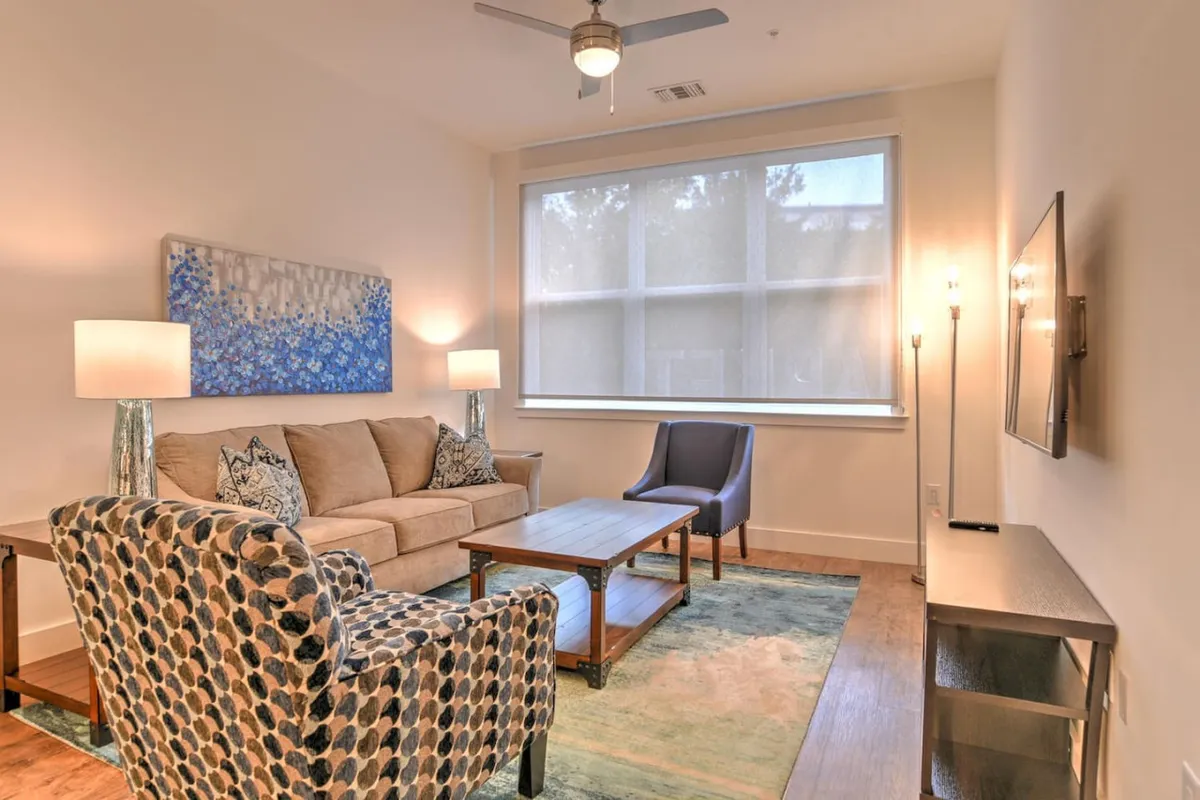 A cozy and modern living room featuring a comfortable sofa, accent chairs, and a stylish coffee table. Wall art and a television add warmth and a personal touch, inviting guests to relax, socialize, or unwind with entertainment after a day in the city.