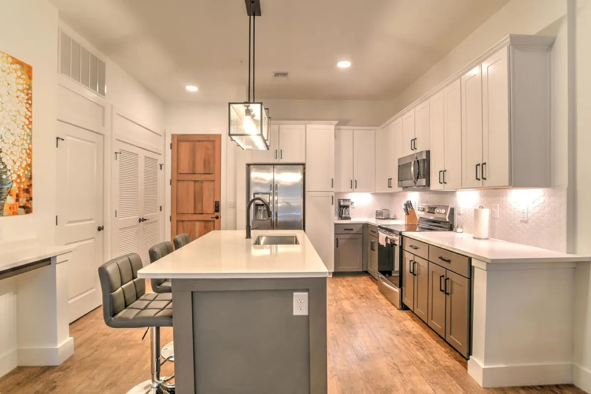 A modern interior scene featuring a welcoming kitchen area with an island countertop, stainless steel appliances, elegant light fixtures, and a sturdy wooden door visible in the background. The door could plausibly represent or symbolize the secure entry to the residence, and the overall space feels functional and accessible.