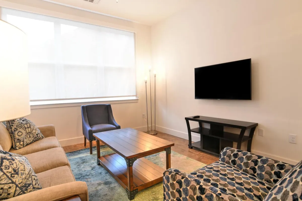 This image showcases a cozy living room with a comfortable sofa, a coffee table positioned for easy gathering, a stylish blue armchair, and a TV mounted for entertainment. The space is clearly designed for group relaxation and socializing, inviting guests to unwind together after exploring the city.