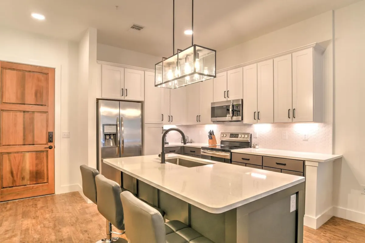 A contemporary kitchen area with a prominent island countertop, hanging light fixture, and gleaming stainless steel appliances. The well-lit space radiates warmth and functionality, perfect for both casual breakfasts and festive dinner parties.