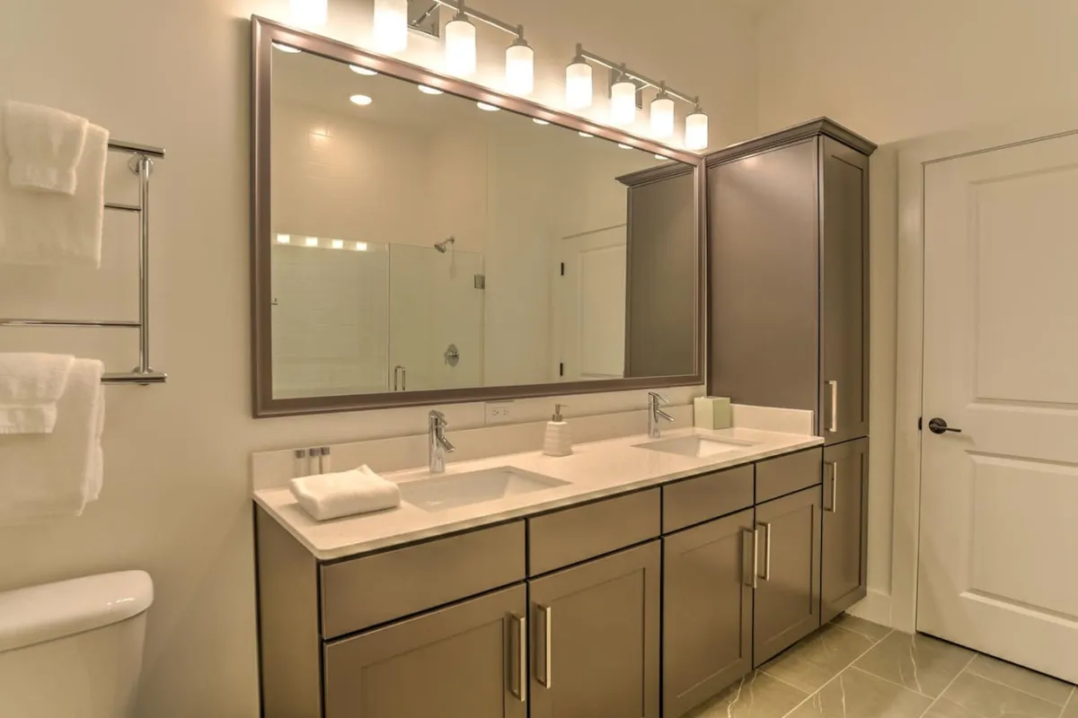 A bright, organized bathroom with a double vanity, large mirror, and warm lighting fixtures. The space is clean and inviting, ideal for refreshing mornings or unwinding after a long workday.