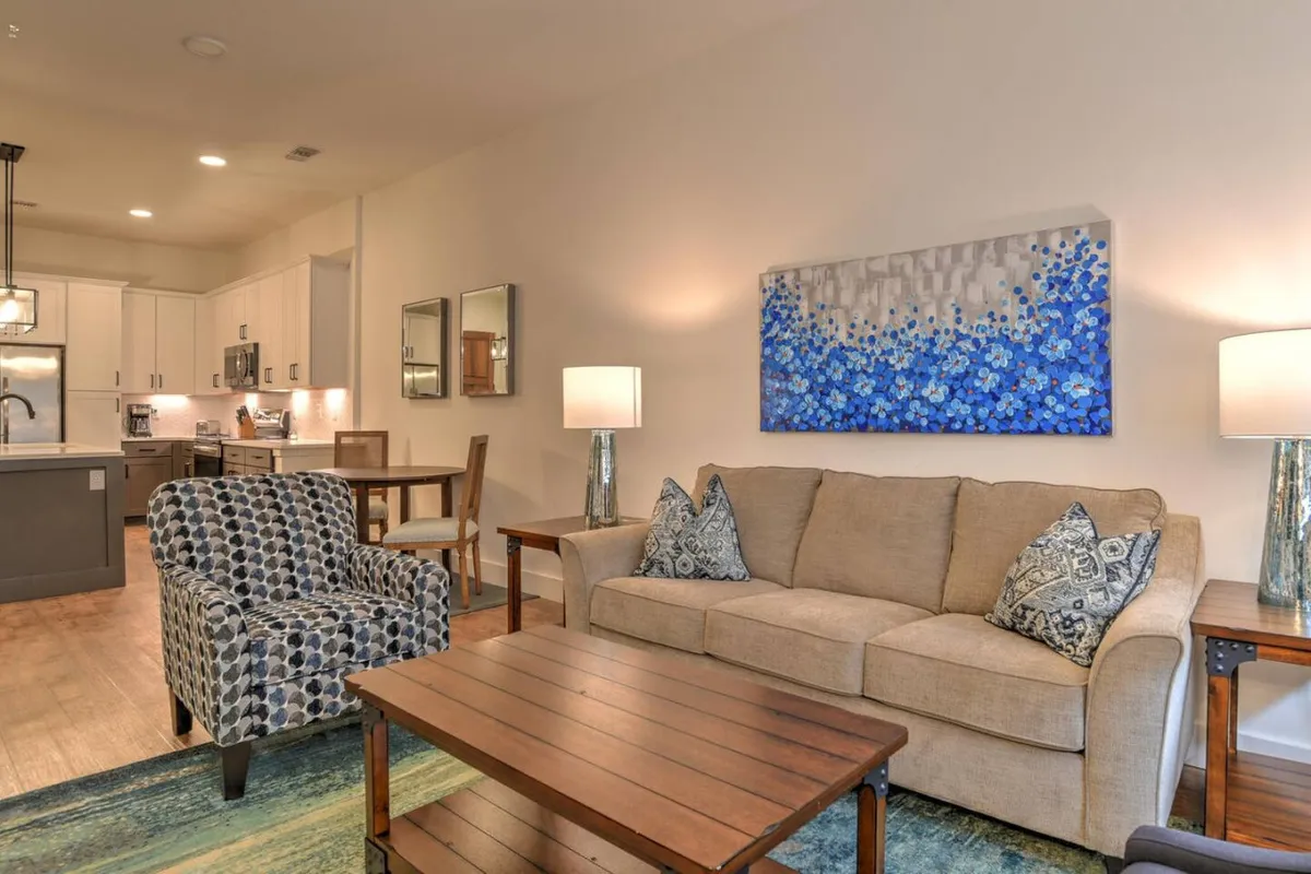 This image features a comfortable, inviting living space with blue floral wall art, a textured armchair, and a natural wood coffee table. The arrangement and decor suggest a modern, urban condo ambiance perfect for relaxing after a day out in the city.