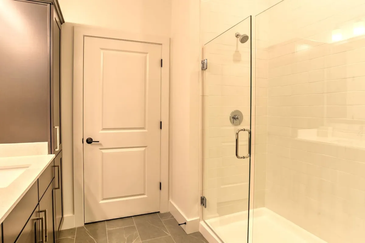 This modern bathroom features a sleek glass shower enclosure, a contemporary vanity with a large mirror, and minimalist cabinetry. The clean lines and ample lighting evoke a spa-like environment, ideal for unwinding after a busy day.