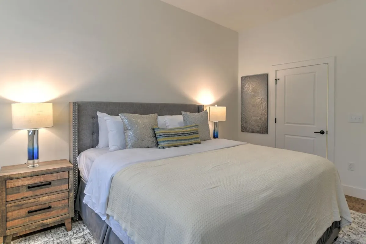 A stylishly appointed bedroom featuring a comfortable king bed adorned with decorative pillows, soft lighting from table lamps, and tasteful artwork on the wall. The calm, uncluttered space offers a tranquil retreat for rest and productivity.